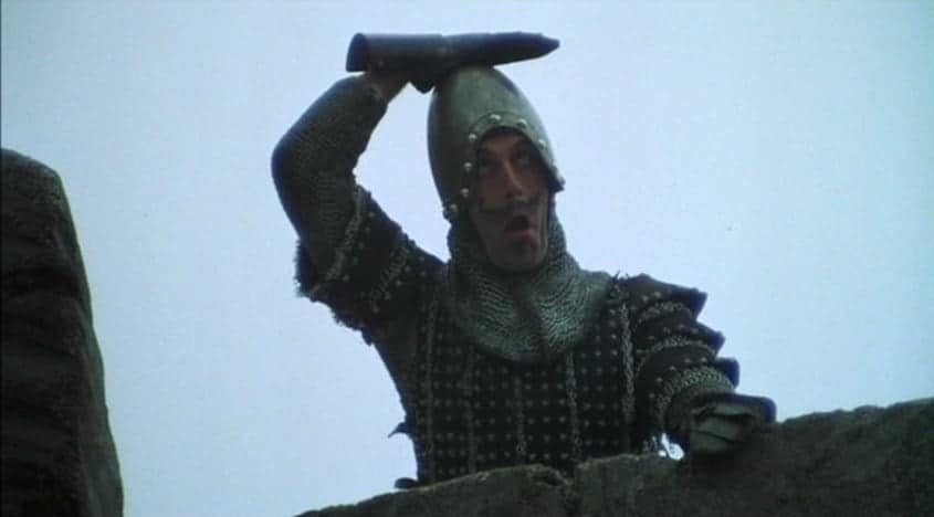 Man behind a wall in armour one presumes it is a castle wall. He is hitting is head with his right hand.